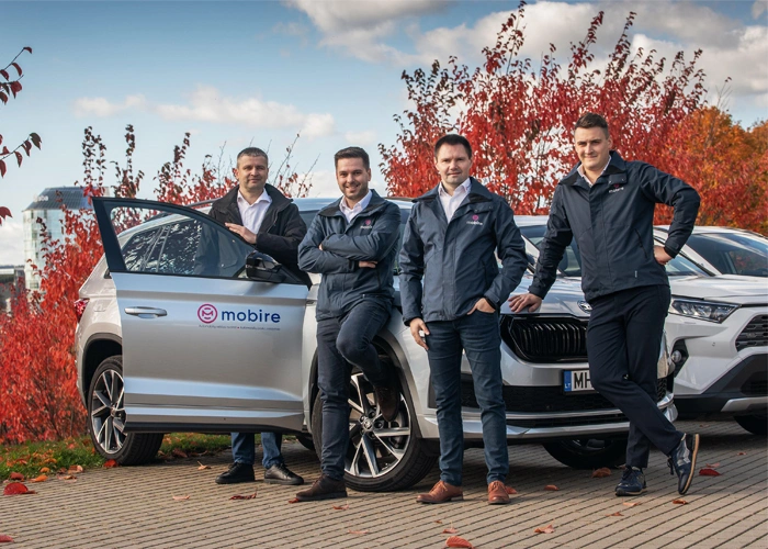 Four members of Mobire standing next to a silver car.